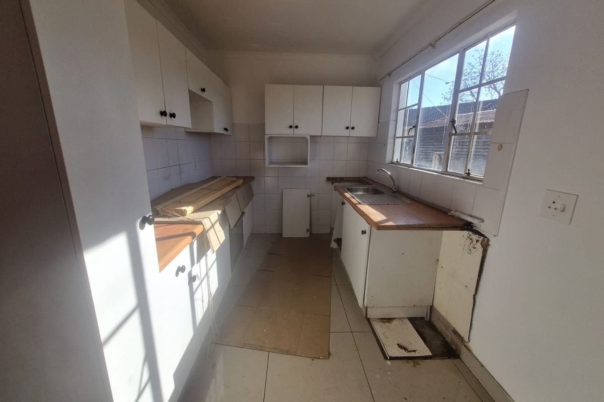 A dated kitchen featuring white cabinetry, laminate countertops, and tiled flooring, currently in need of renovation and repair to restore functionality.