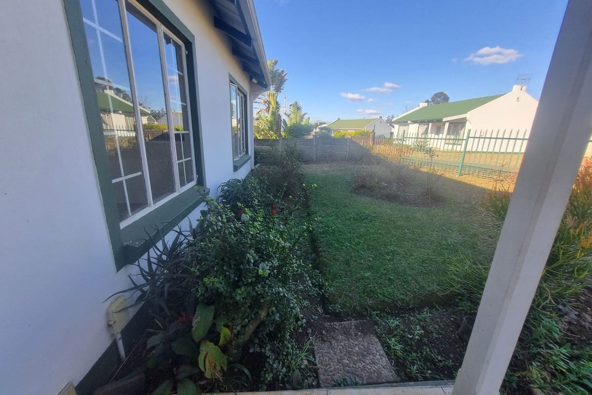 A view of the rear garden and lawn area, featuring a tiled patio and metal perimeter fencing.