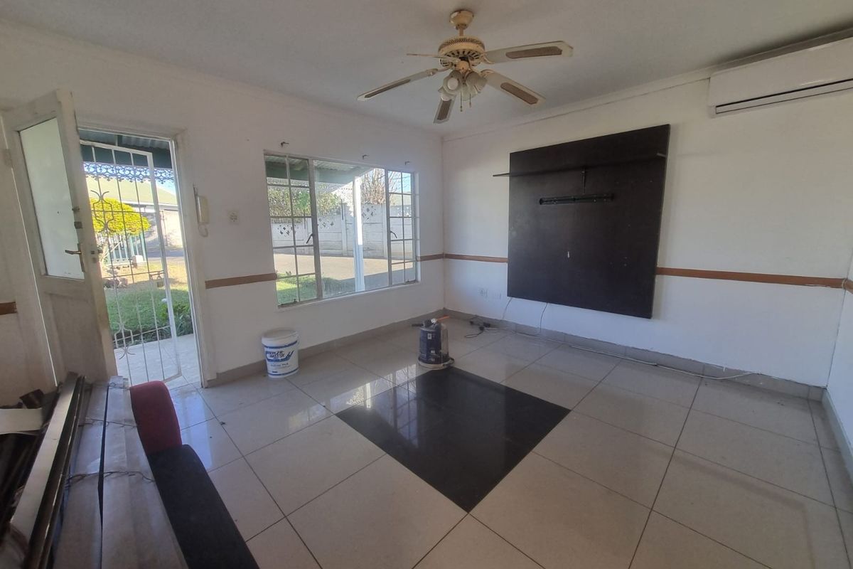 An empty living room featuring tiled floors, a ceiling fan, an air conditioning unit, and a built-in wall panel with direct access to the garden.
