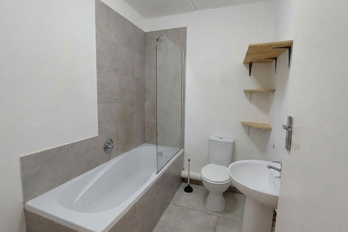 A clean, functional bathroom featuring a bathtub with a glass screen, a pedestal basin, and a standard toilet with neutral wall tiling.