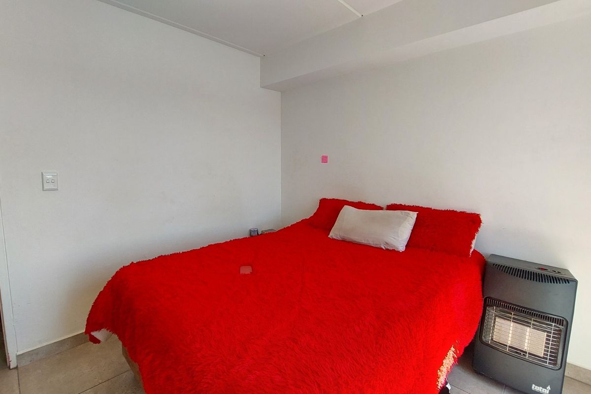 A simple bedroom featuring tiled flooring and neutral white walls, providing a functional and blank canvas for personalization.