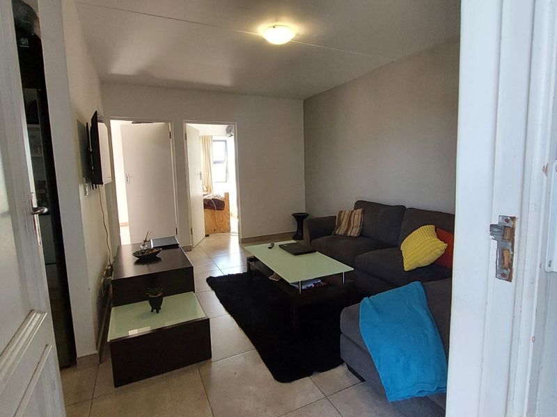 A compact living room featuring tiled flooring and neutral wall finishes, providing a functional space with access to adjacent rooms.