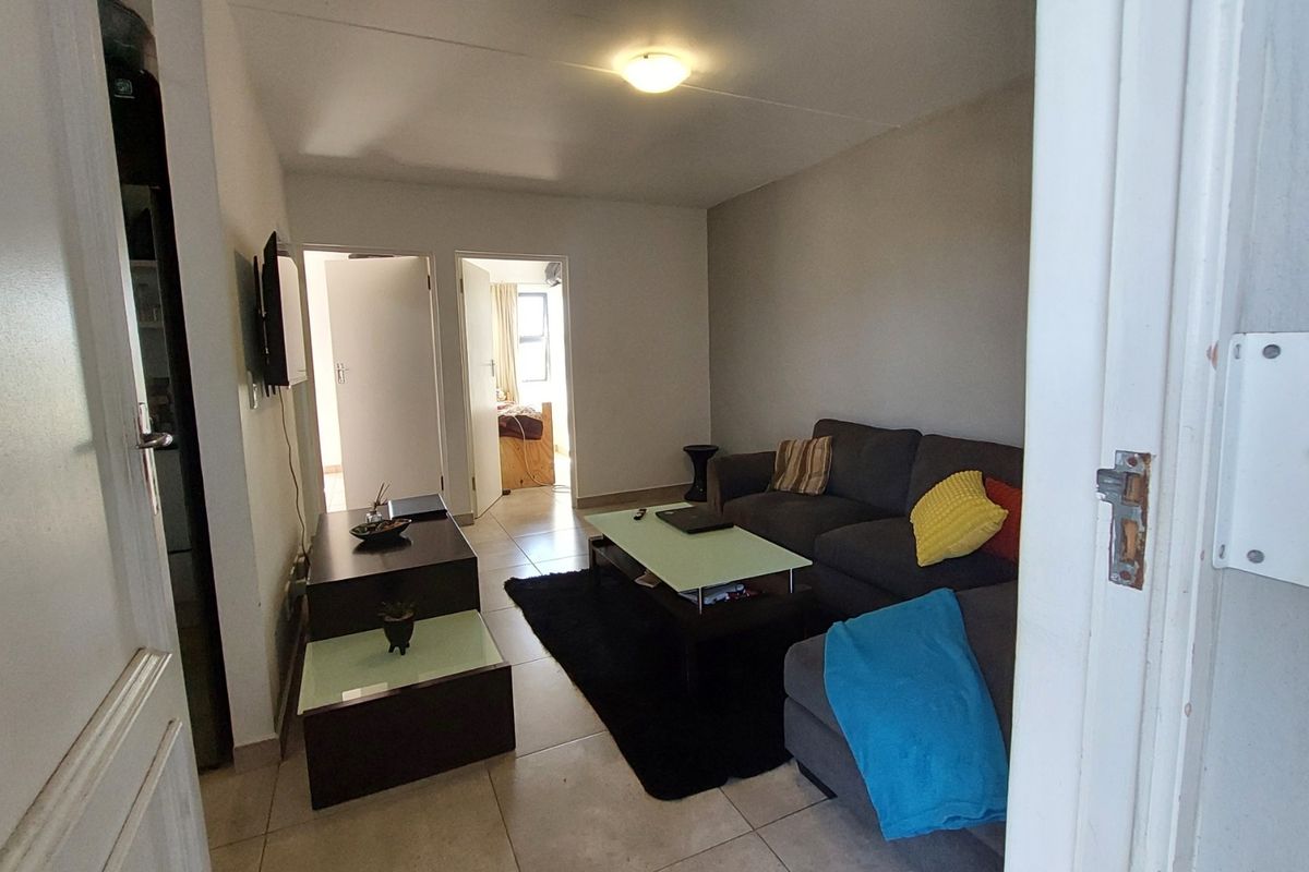 A compact living room featuring tiled flooring and neutral wall finishes, providing a functional space with access to adjacent rooms.