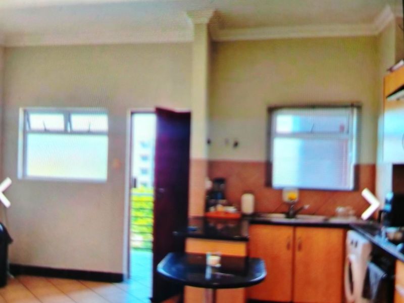 A functional kitchen area featuring built-in cabinetry, laminate countertops, and tiled flooring, with direct access to an outdoor balcony space.