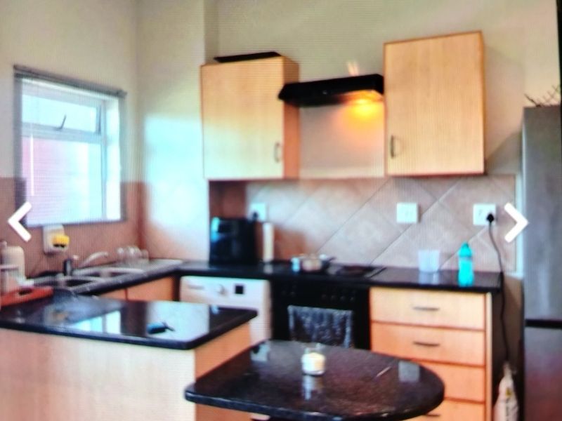 A functional kitchen featuring light wood cabinetry, dark granite countertops, a breakfast nook, and tiled flooring with a built-in oven and extractor fan.