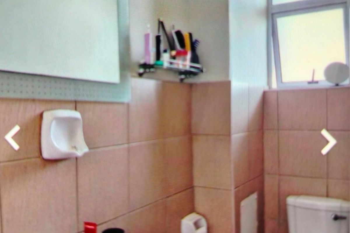 A compact bathroom featuring a wall-mounted basin, toilet, and tiled walls, requiring cosmetic updates to improve its dated appearance.