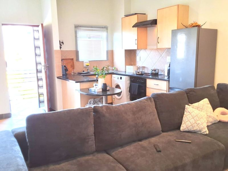 Open plan living area featuring a compact kitchen with built-in cabinetry, tiled backsplash, and direct access to an exterior door.