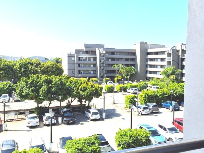 Elevated view overlooking the apartment complex parking area and surrounding landscaped grounds, captured from a balcony.