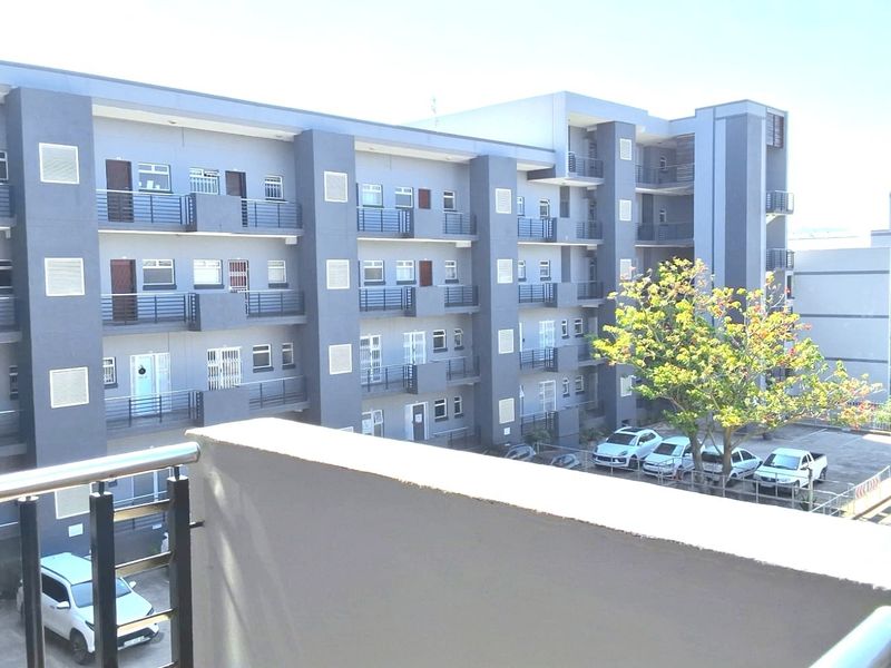A view of the apartment complex exterior, featuring multi-story residential units with private balconies and an adjacent parking area.