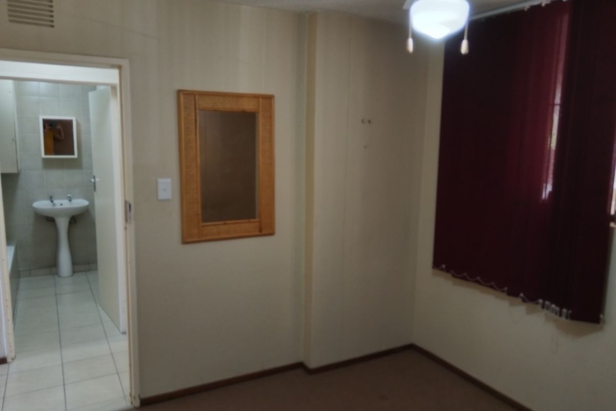 An empty bedroom featuring carpeted flooring, a ceiling fan, and an adjoining bathroom with a pedestal basin.