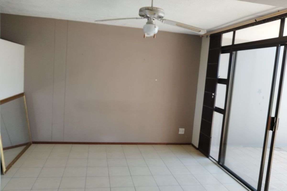An empty living room featuring tiled flooring, a ceiling fan, and a large sliding glass door providing access to an outdoor area.