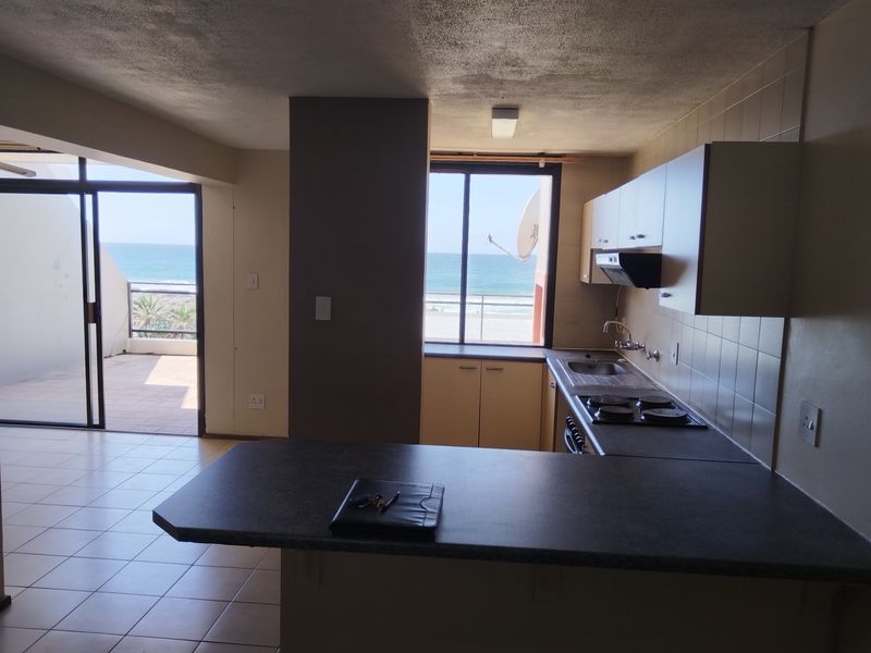 Open-plan kitchen and living area featuring tiled floors, built-in cabinetry, and direct access to a balcony with ocean views.