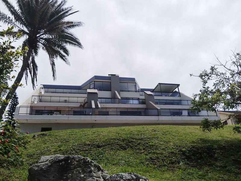 Rear elevation of a multi-story apartment building featuring tiered balconies with glass balustrades and large sliding glass doors.