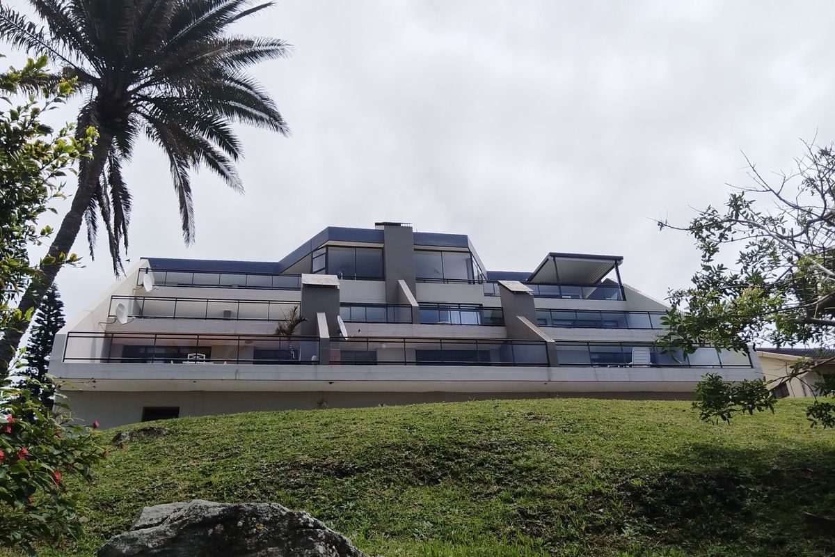 Rear elevation of a multi-story apartment building featuring tiered balconies with glass balustrades and large sliding glass doors.