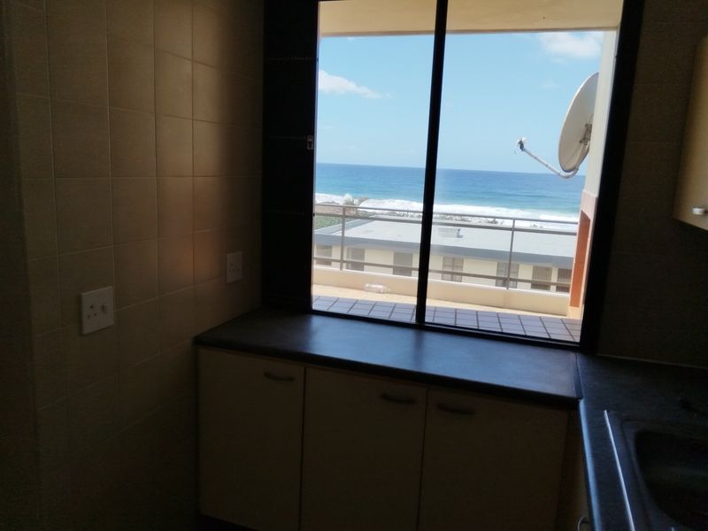 A functional kitchen area featuring built-in cabinetry and a tiled splashback, offering a direct view of the ocean through a large sliding window.