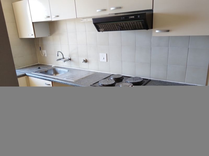 A functional kitchen featuring laminate cabinetry, a stainless steel sink, tiled backsplash, and a built-in electric hob with an extractor fan.