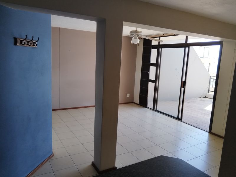 An open-plan living area featuring tiled flooring, a ceiling fan, and large sliding glass doors that provide access to an outdoor balcony space.