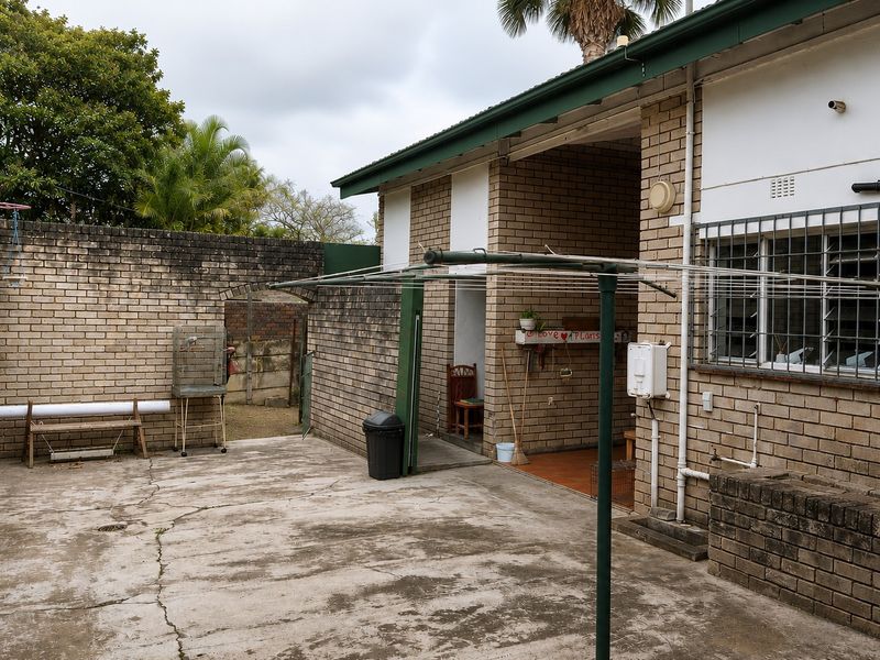 Rear exterior area featuring brick masonry walls, concrete paving, and a covered patio section, showing signs of age and weathering.