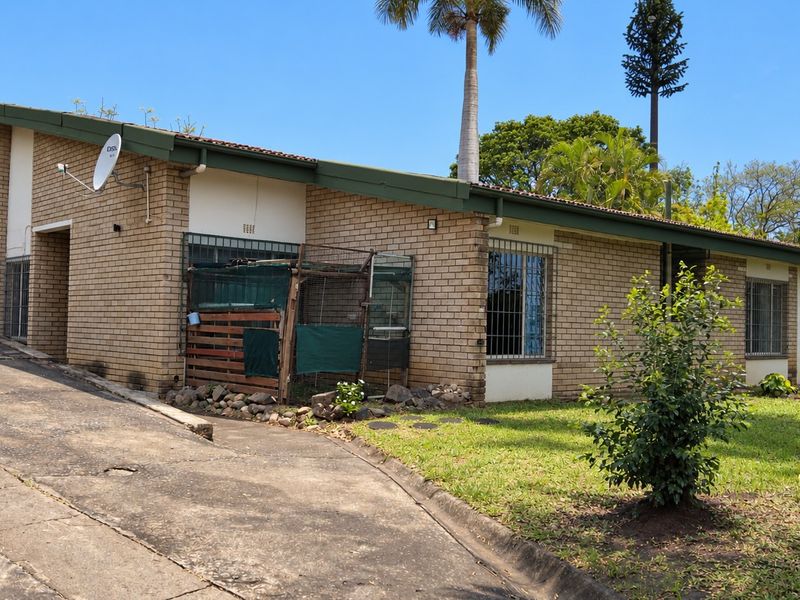 Front exterior view of a single-story brick house featuring a concrete driveway, security bars on windows, and a tiled roof.