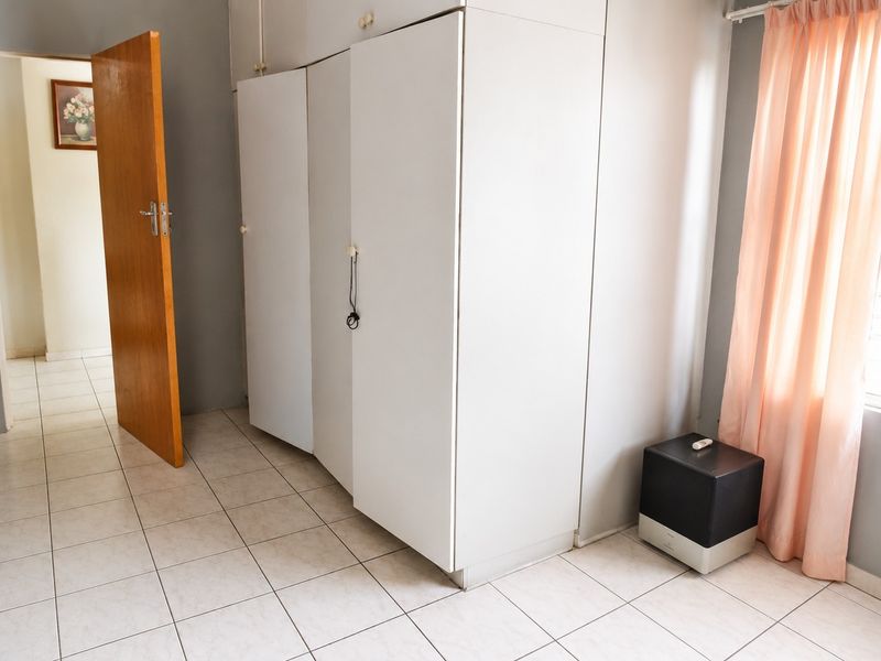 A bedroom featuring built-in cupboards, tiled flooring, and a timber door, offering a functional space ready for personalization.