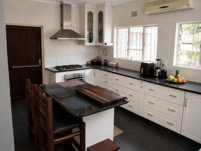 A functional kitchen featuring white cabinetry, dark granite countertops, a gas hob with extractor fan, and tiled flooring with integrated air conditioning.