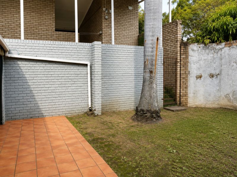 Rear exterior area featuring a tiled patio, brick walling, and a small garden space with a mature tree.