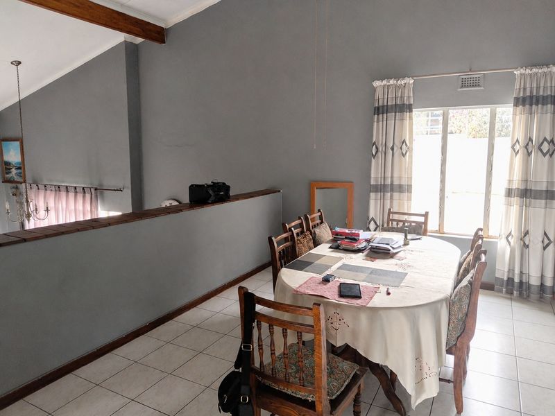 A dining area featuring tiled flooring, a vaulted ceiling with an exposed timber beam, and a large window providing natural light.
