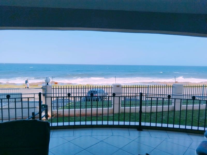 A covered balcony featuring tiled flooring and a metal balustrade, offering direct views of the ocean and coastal road.