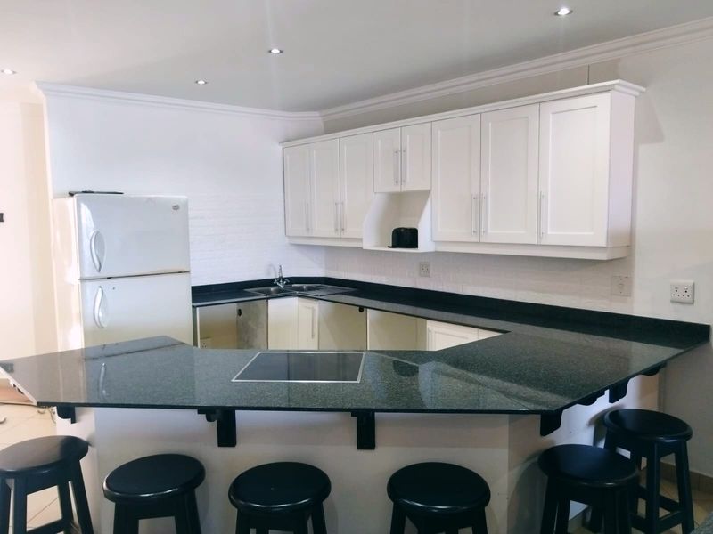 Kitchen featuring white cabinetry, dark granite countertops, and an integrated breakfast bar with an inset electric hob.