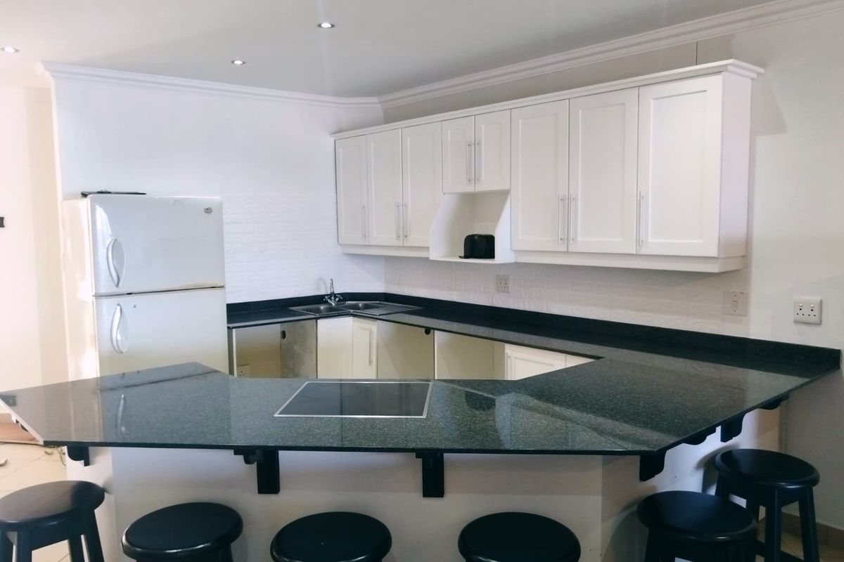 Kitchen featuring white cabinetry, dark granite countertops, and an integrated breakfast bar with an inset electric hob.