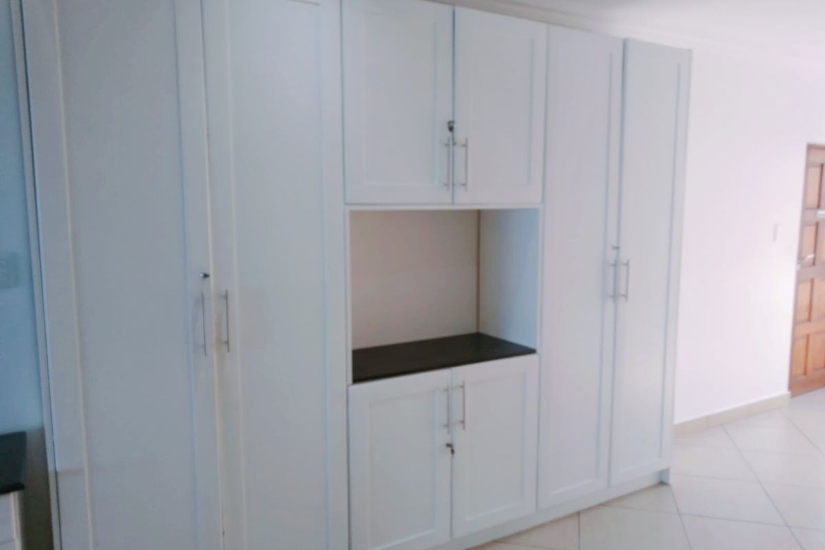 A clean, well-maintained bedroom featuring ample white built-in cupboards with modern hardware and neutral tiled flooring.
