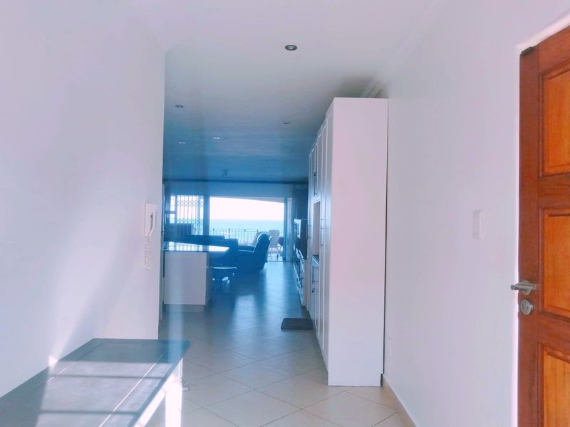 An entrance hallway featuring tiled flooring, built-in storage cabinetry, and recessed lighting, leading into an open-plan living area with ocean views.