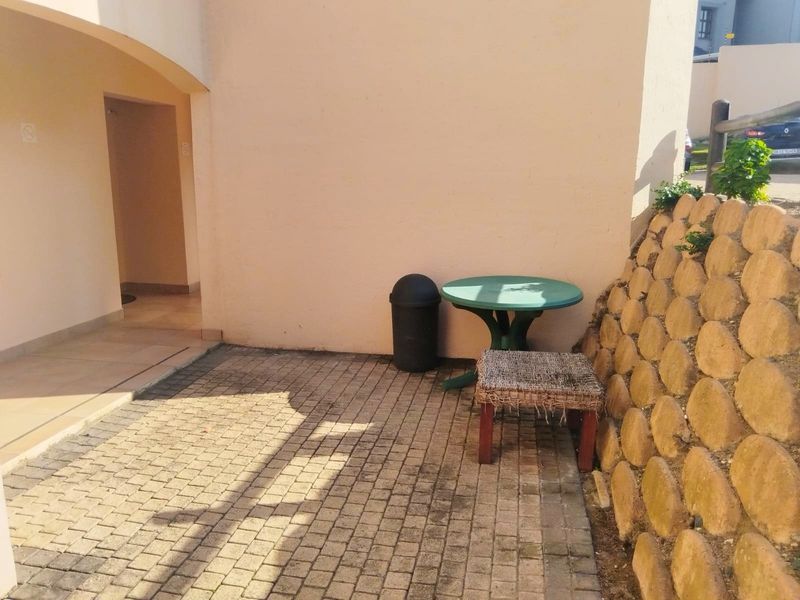 A paved rear patio area featuring a stone retaining wall and an arched entrance to the apartment.