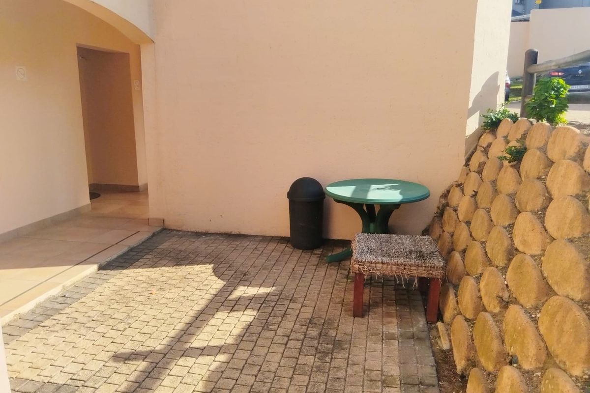A paved rear patio area featuring a stone retaining wall and an arched entrance to the apartment.