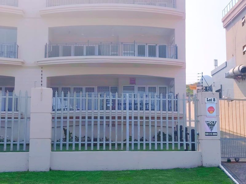 Front elevation of a multi-story apartment building featuring balconies, secure perimeter fencing with electric wire, and gated access.