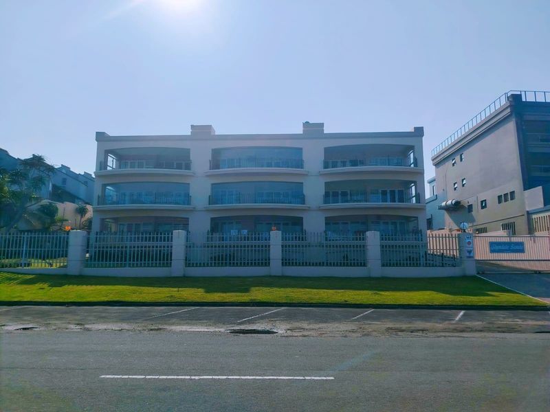Front elevation of the Glyndale Sands apartment complex, featuring multi-level balconies, secure perimeter fencing, and a paved street-level parking area.