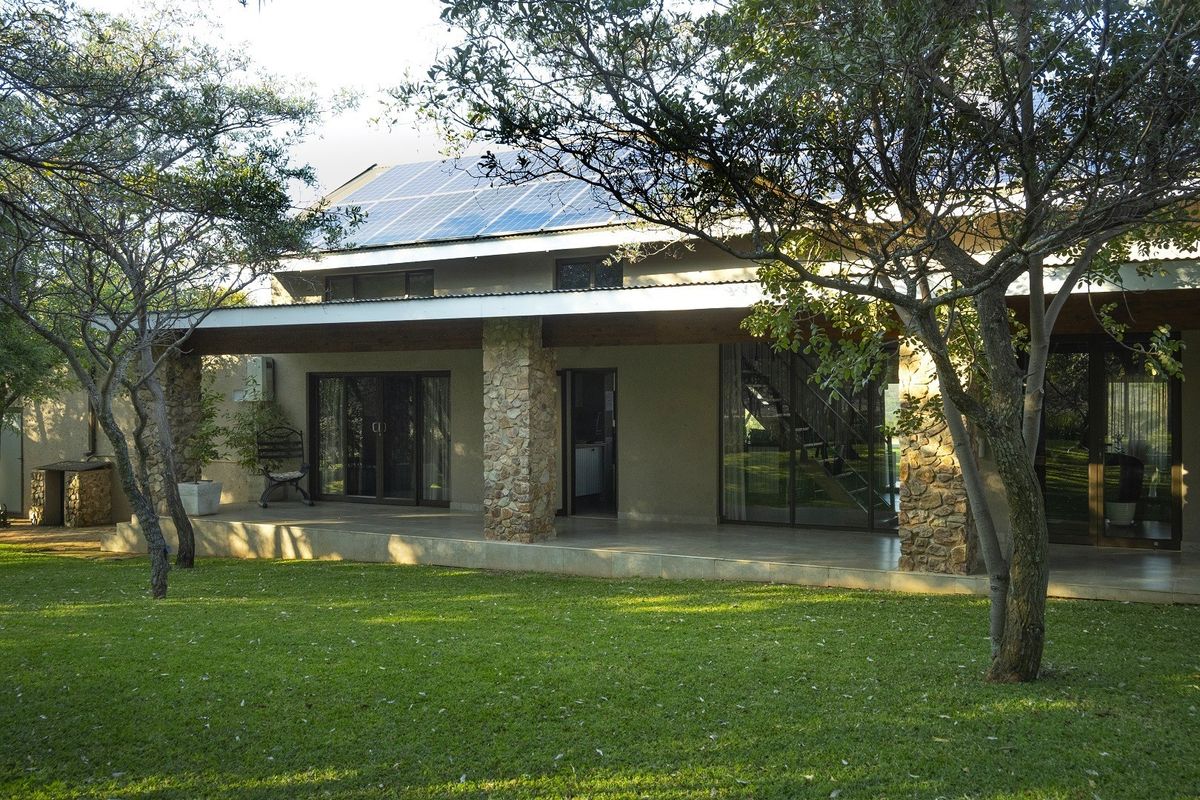 Rear view of the property featuring a spacious covered patio with stone-clad pillars, large sliding glass doors, and roof-mounted solar panels.