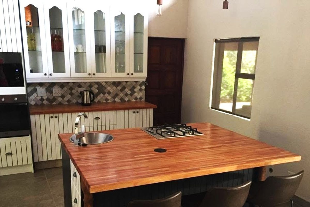 A well-appointed kitchen featuring a central island with a wooden countertop, integrated gas hob, built-in oven, microwave, and ample cabinetry with a tiled backsplash.