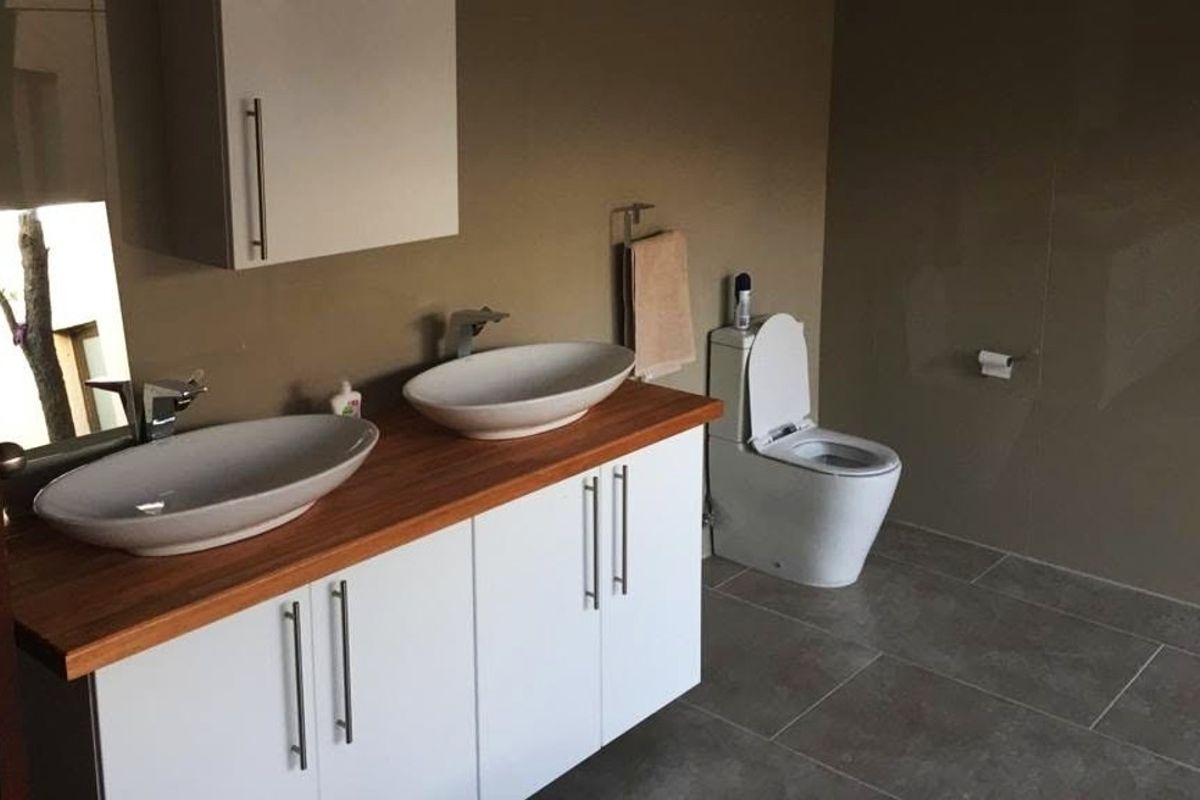 Modern bathroom featuring a double vanity with vessel sinks, wooden countertop, built-in white cabinetry, and tiled finishes throughout.