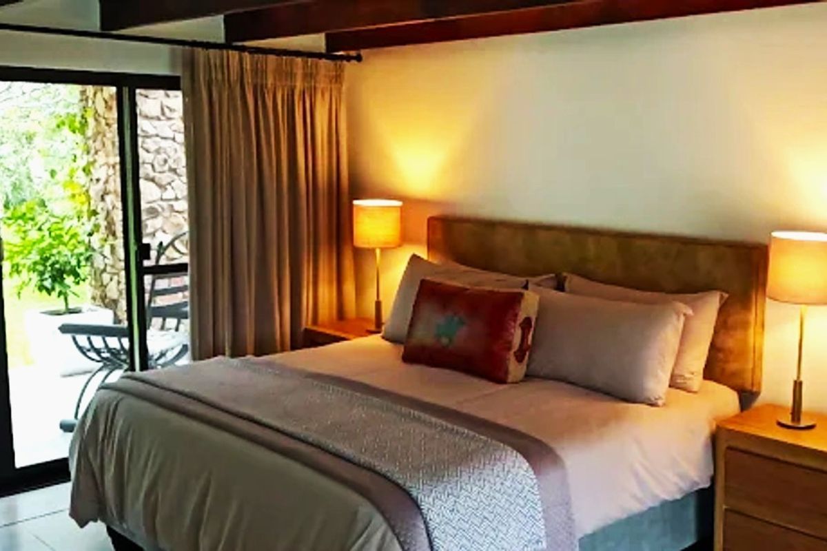 A cozy bedroom featuring exposed timber ceiling beams and a sliding glass door providing direct access to the outdoor patio area.