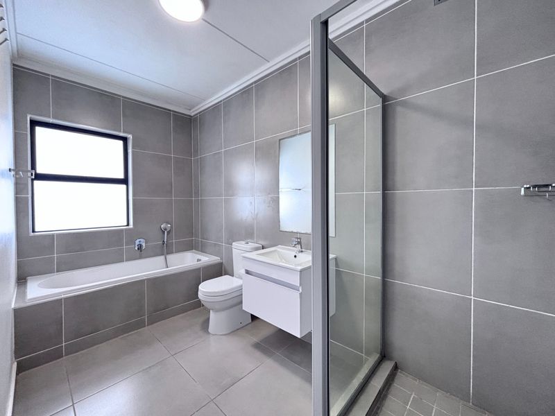 Modern bathroom featuring large format grey wall and floor tiles, a built-in bathtub, a glass-enclosed shower, and a contemporary wall-mounted vanity.