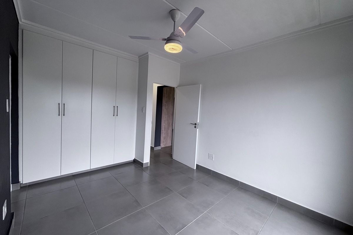 A clean, empty bedroom featuring modern grey floor tiles, built-in white cupboards, and a ceiling fan.