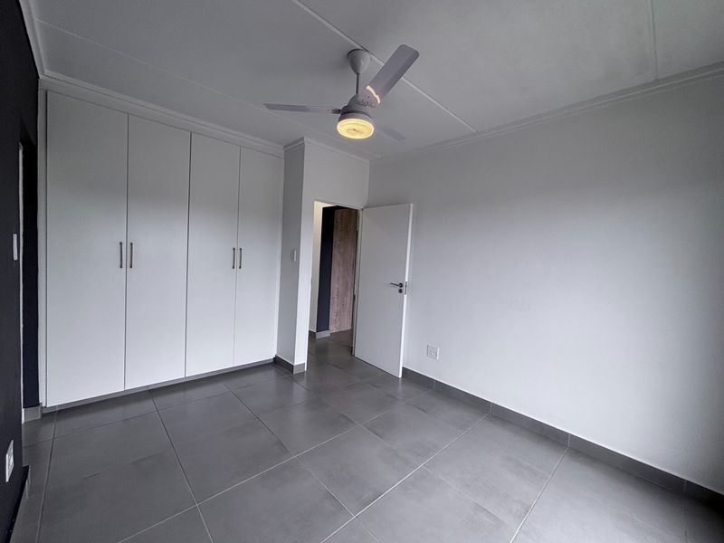 A clean, empty bedroom featuring modern grey floor tiles, built-in white cupboards, and a ceiling fan.