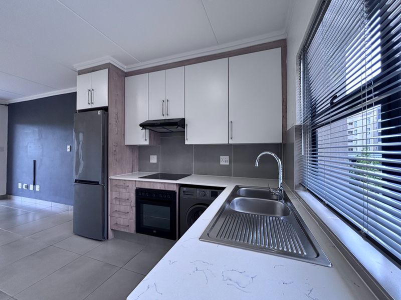 Modern kitchen featuring white and wood-grain cabinetry, integrated appliances, a stainless steel sink, and tiled flooring with a neutral color palette.