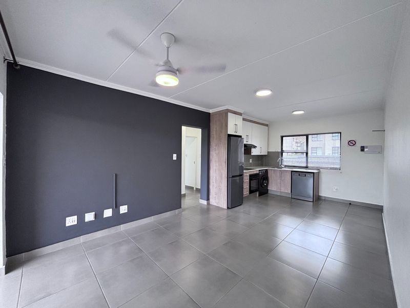 Spacious open-plan living area featuring modern tiled flooring, a ceiling fan, and a functional kitchen with built-in cabinetry and integrated appliances.