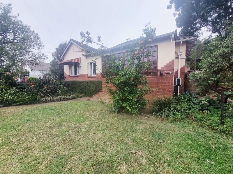 Front elevation of a traditional brick house featuring a tiled roof, casement windows, and established garden surroundings.