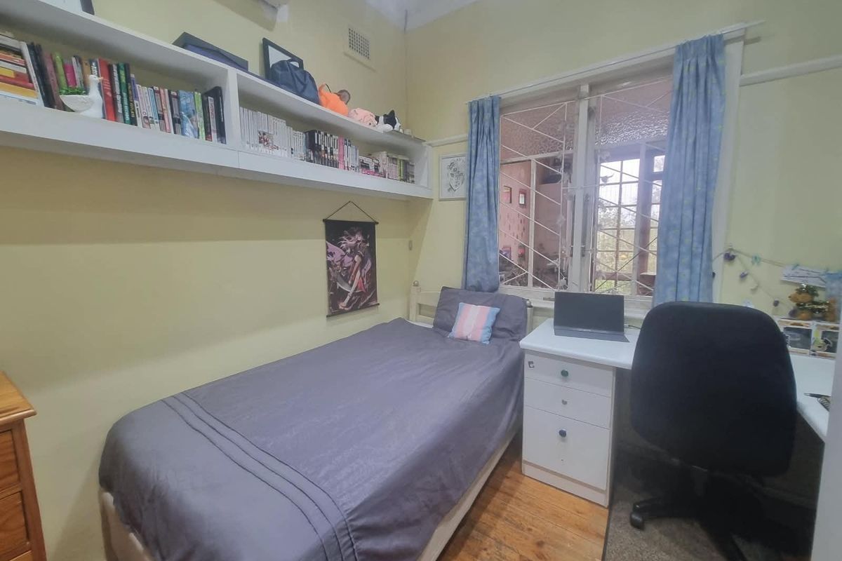 A functional bedroom featuring timber flooring, built-in wall shelving, and a split-system air conditioner for climate control.