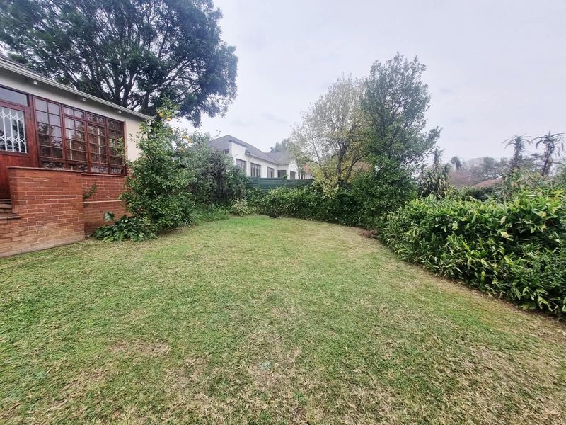 A private rear garden featuring a well-maintained lawn, established perimeter hedging, and a view of the brick-clad exterior of the house.
