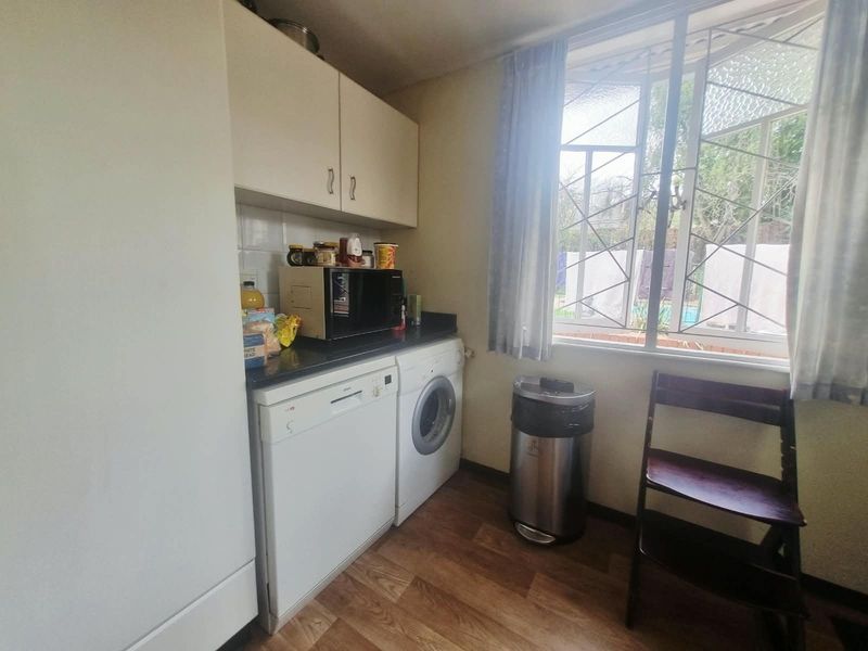 Functional laundry area featuring built-in cabinetry, tiled backsplash, and space for under-counter appliances, with natural light from a window with security bars.