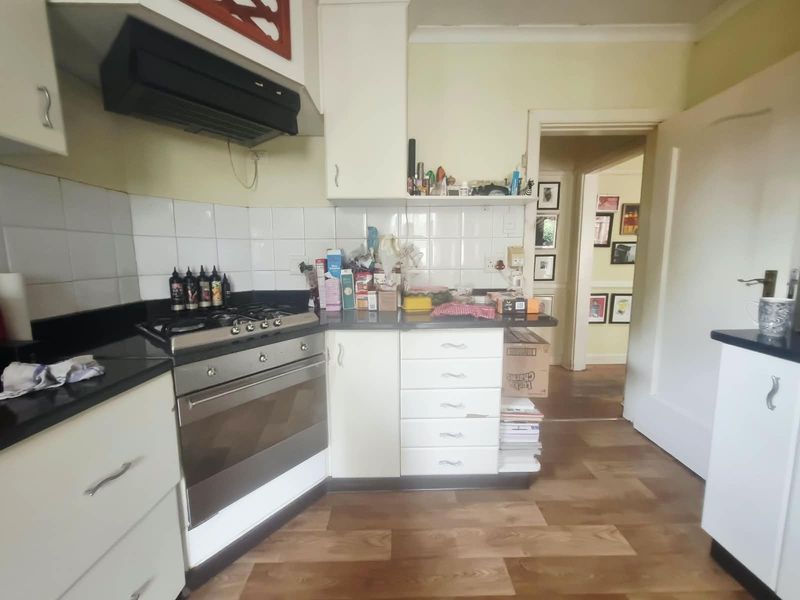 A functional kitchen featuring built-in cabinetry, a gas hob with extractor fan, and tiled backsplash, leading into an adjacent hallway.